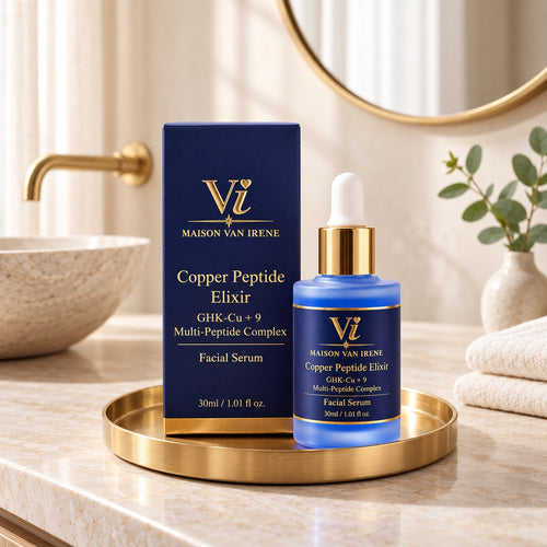 Maison Van Irene Copper Peptide Elixir bottle and navy carton on a brushed-brass tray, on a stone bathroom vanity in morning light